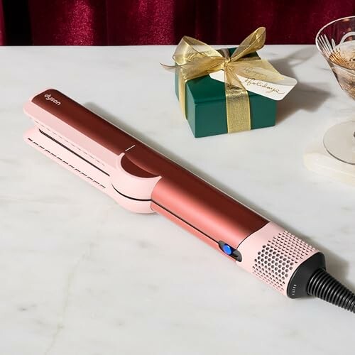 Hair straightener on table with gift box.