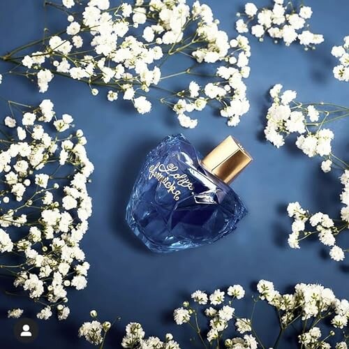 Blue perfume bottle surrounded by baby's breath flowers on a blue background.