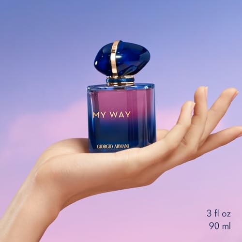 Hand holding Giorgio Armani My Way perfume bottle against a pastel sky background.