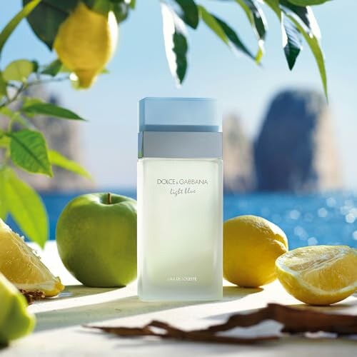 Light Blue perfume bottle surrounded by apples and lemons near the sea.