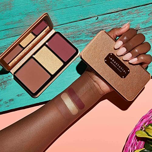 A hand holding a makeup palette with swatches on the arm.