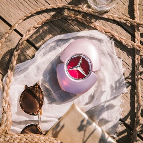 Sunglasses and perfume bottle on a cloth with a woven bag outdoors.