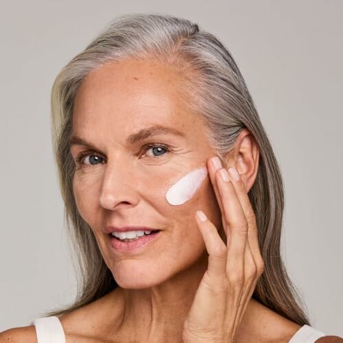 Woman applying face cream to cheek