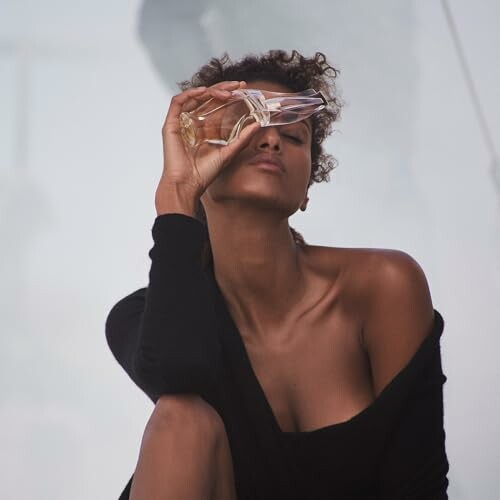 Woman holding eyewear with eyes closed, enjoying the scent of Donna Karan Cashmere Mist.