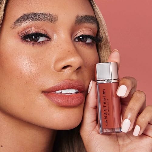 Woman holding a lipstick container close to her face with a matching lip color