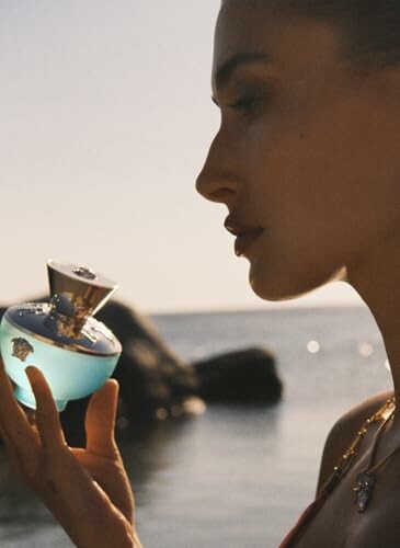 Woman holding a blue perfume bottle by the sea.